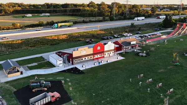 Aerial view of the red barn-style main building, lawn and two vintage trucks at Kackleberry Farms beside a highway